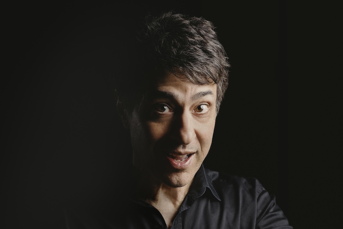 Portrait of stand-up comedian Arj Barker against a dark background.